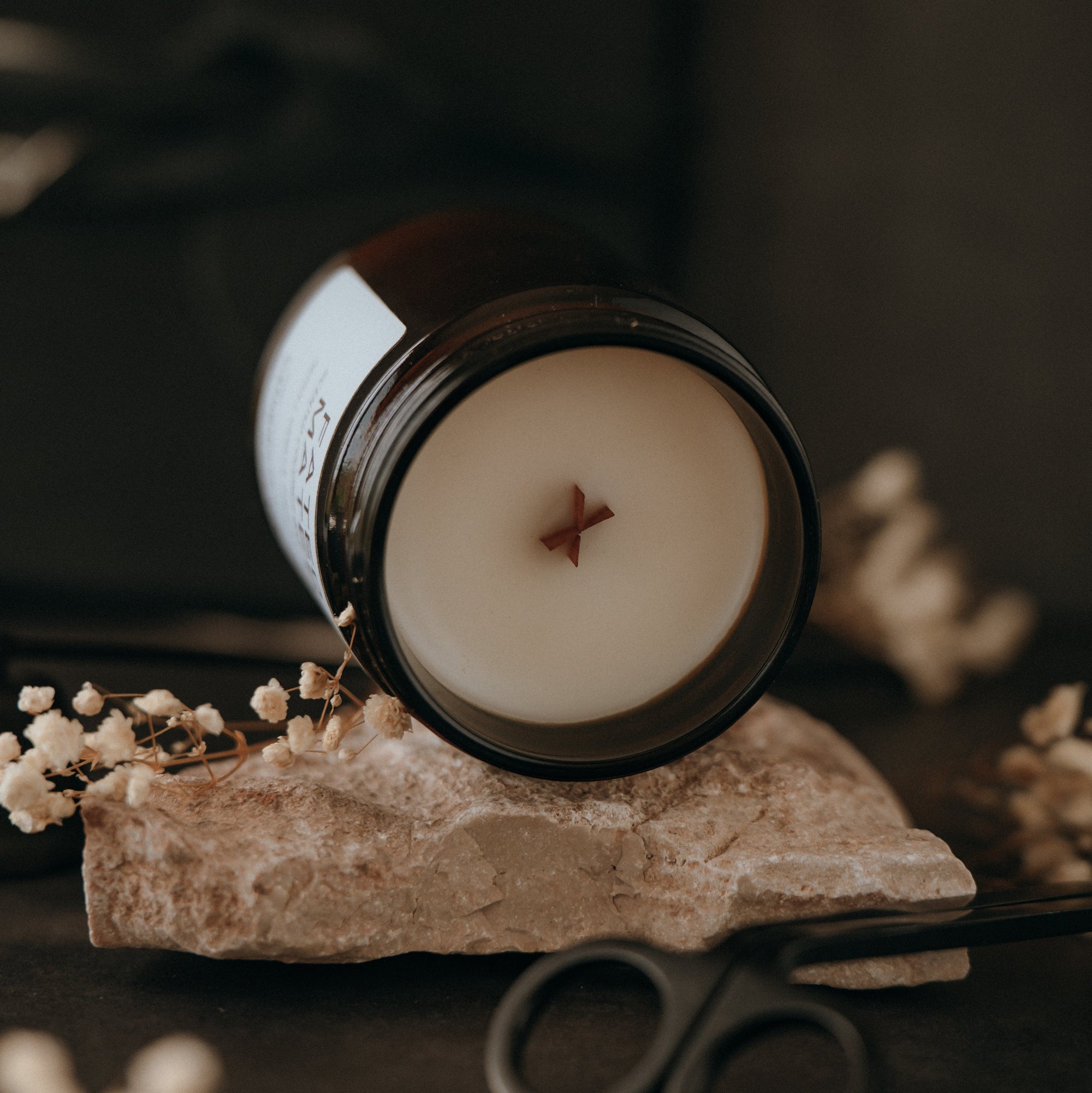 Candle in a glass jar on a stone block with scissors and dried flowers in the background