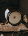Candle in a glass jar on a stone block with scissors and dried flowers in the background