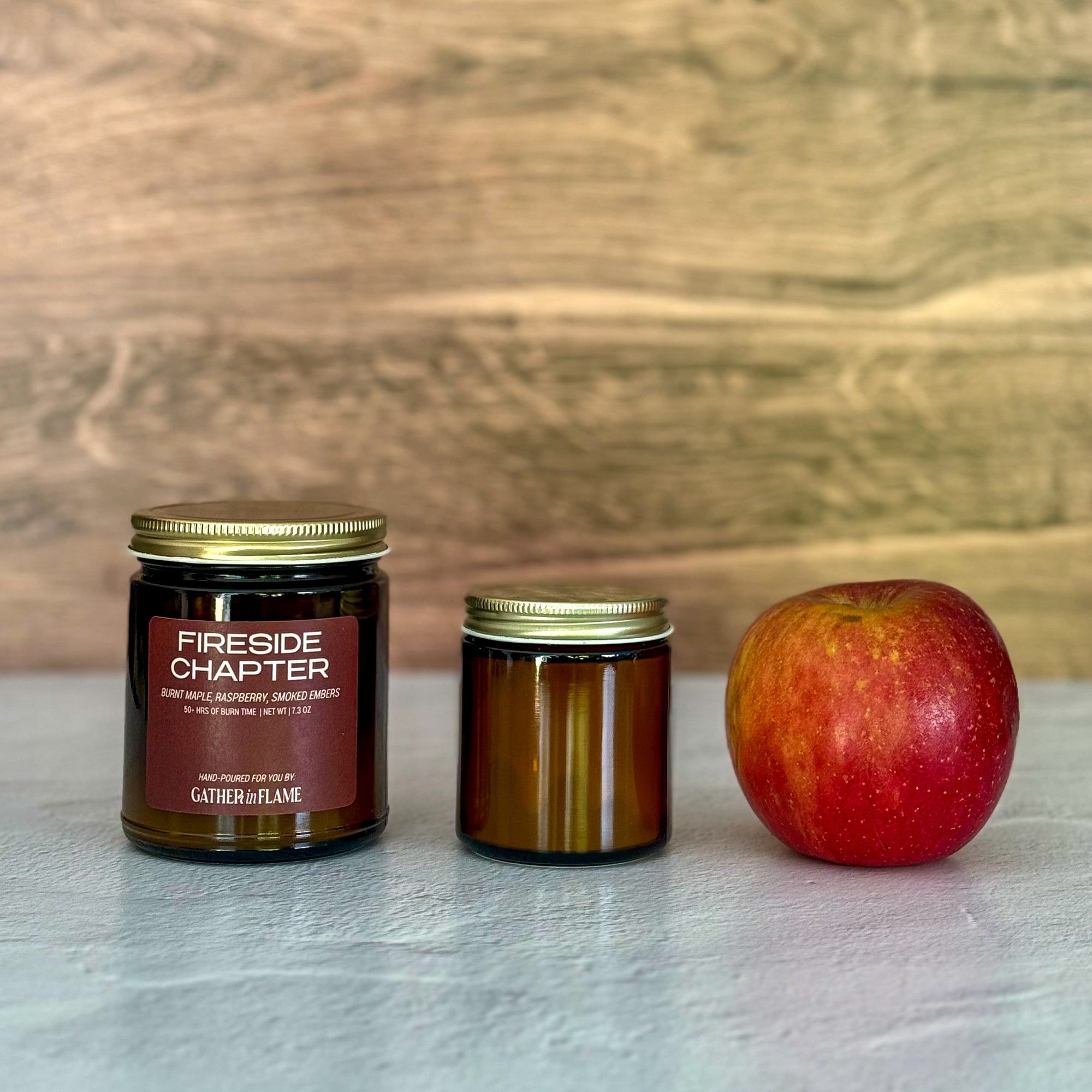 Two candles of different sizes and an apple on a light surface with a wooden background