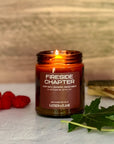 Lit candle labeled 'Fireside Chapter' with raspberries and leaves on a wooden surface