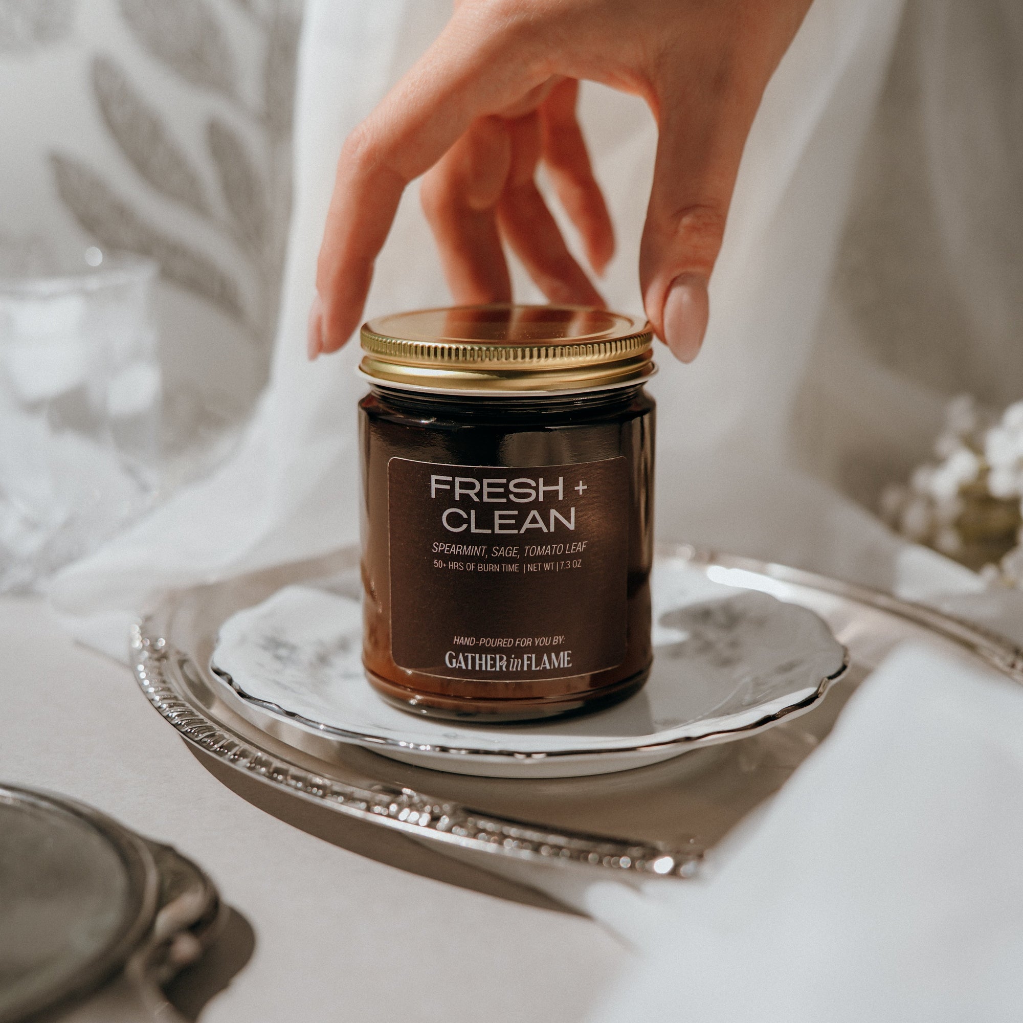 Jar of 'Fresh + Clean' candle on a silver tray with a hand reaching towards it.