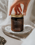 Jar of 'Fresh + Clean' candle on a silver tray with a hand reaching towards it.