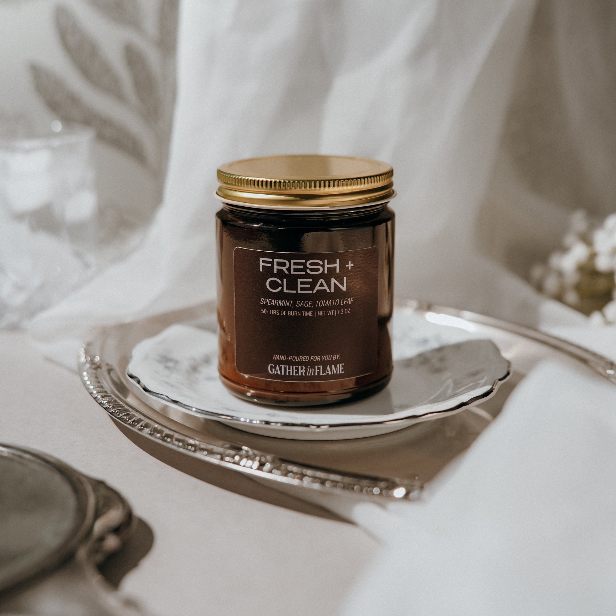 Jar of 'Fresh + Clean' candle on a silver tray with a white fabric background