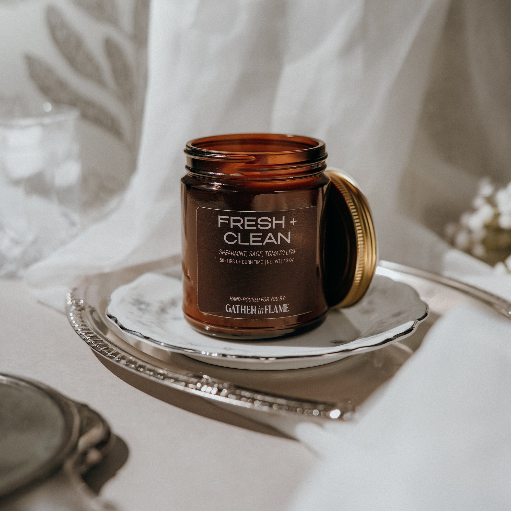 Brown candle jar labeled 'Fresh &amp; Clean' on a white surface with a white curtain background