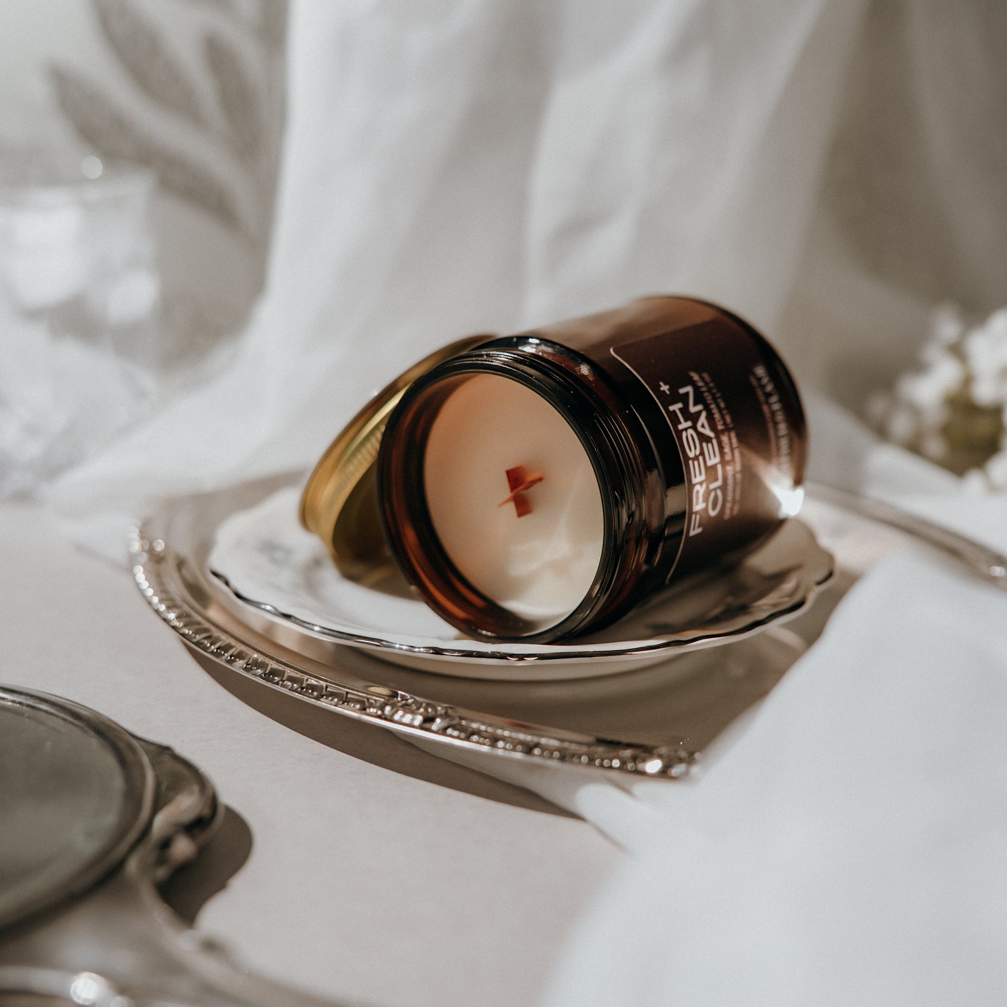 Candle in a decorative container on a white surface with a blurred background