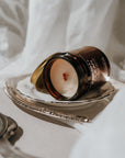 Candle in a decorative container on a white surface with a blurred background