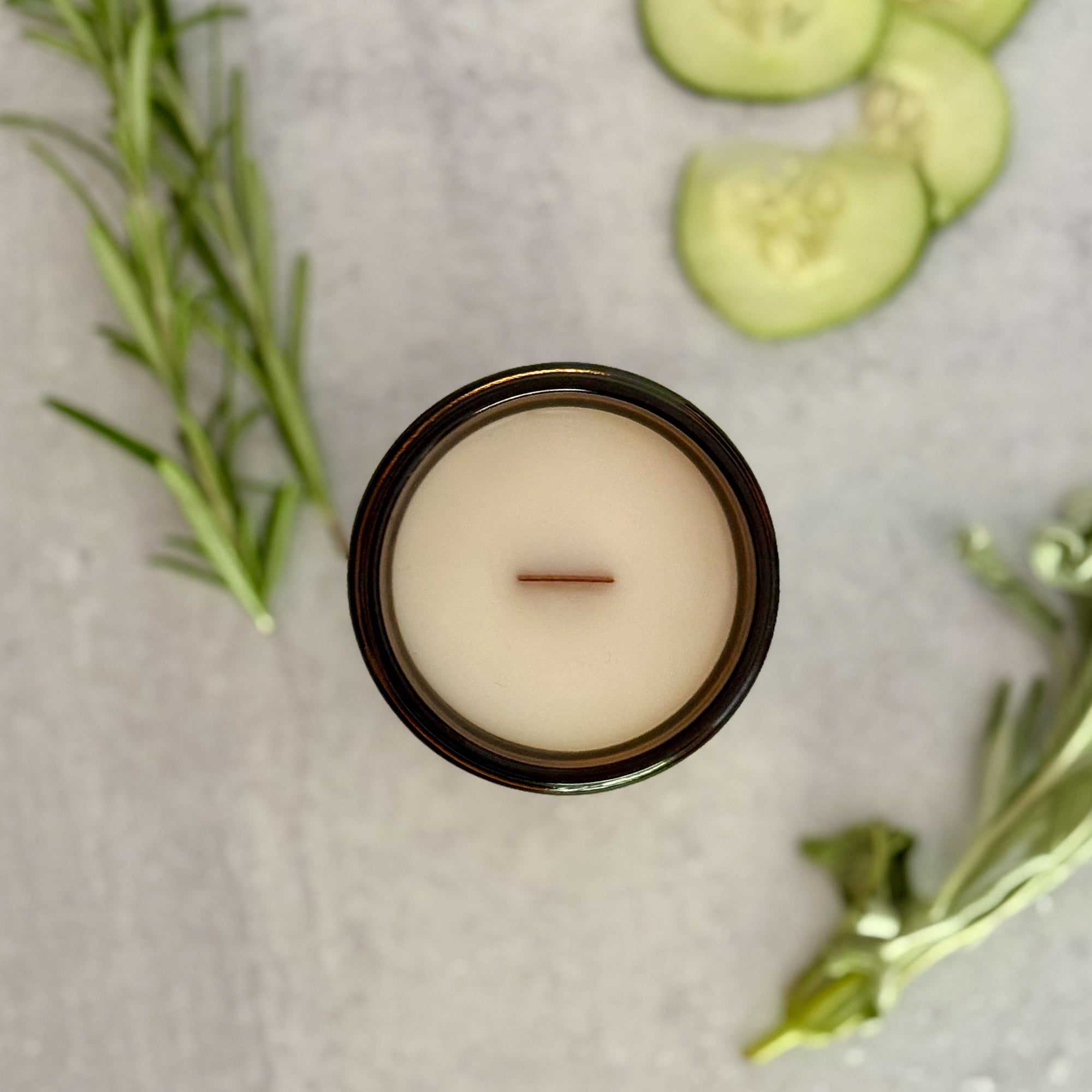 Candle in a glass jar topdown view with cucumber slices and rosemary on a light surface