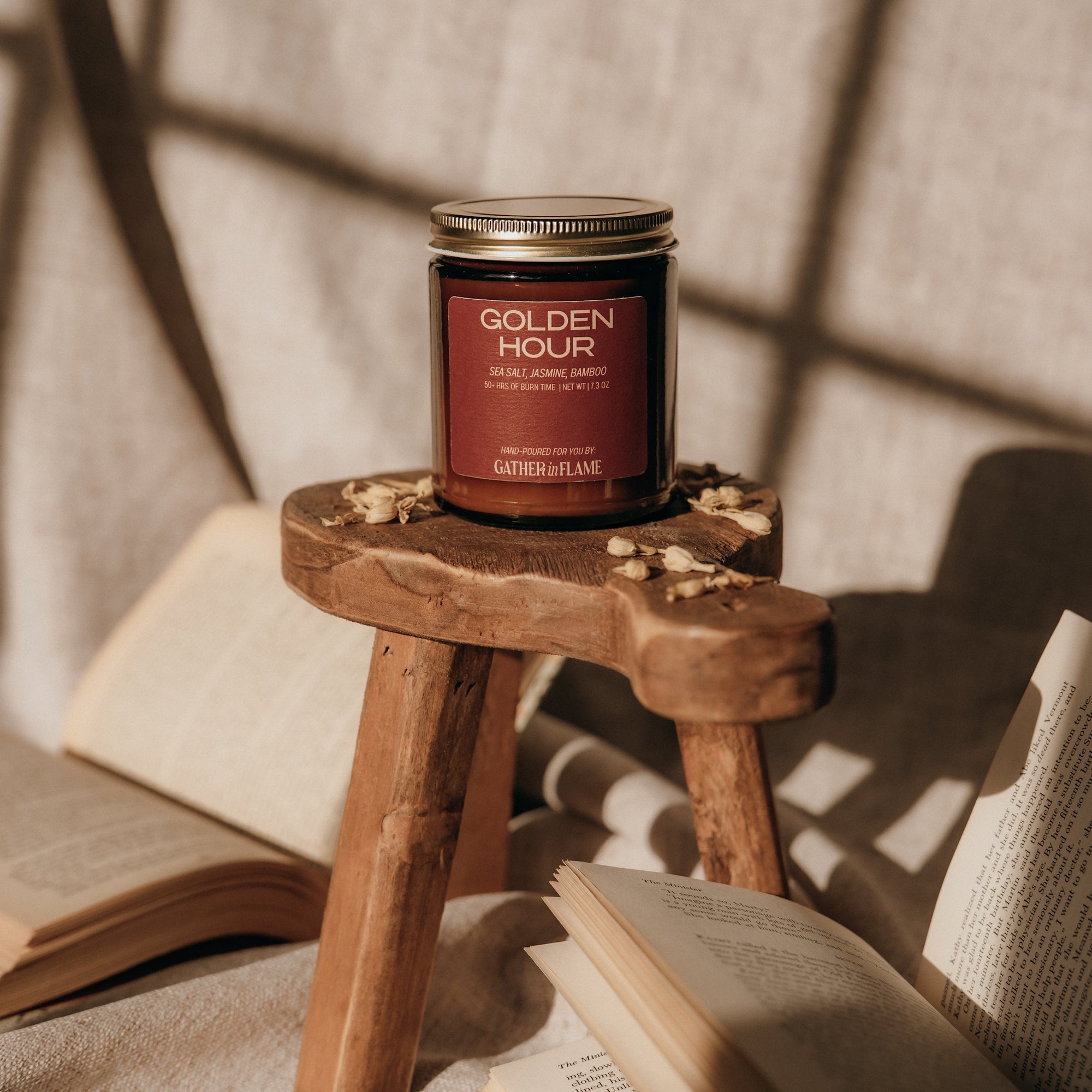 Candle labeled 'Golden Hour' on a small wooden stool with books and a textured wall in the background