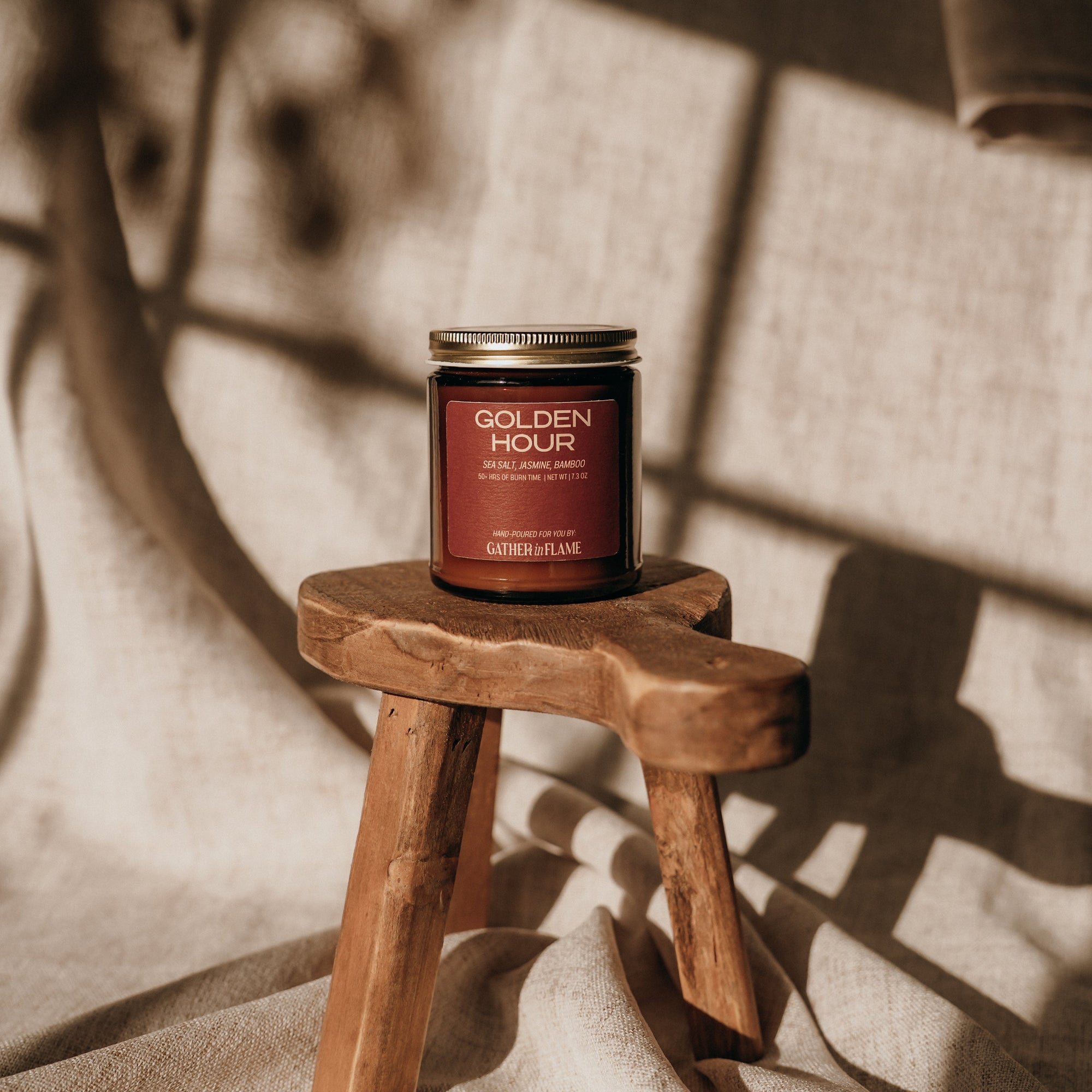 Candle labeled 'Golden Hour' on a small wooden stool with a textured wall background