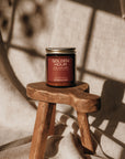 Candle labeled 'Golden Hour' on a small wooden stool with a textured wall background