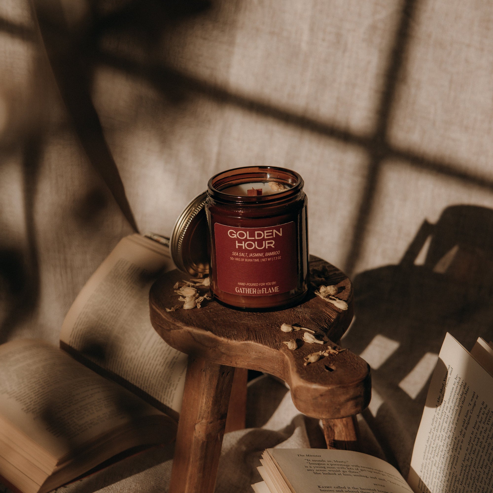 Candle labeled 'Golden Hour' on a small wooden stool with books and fabric in the background