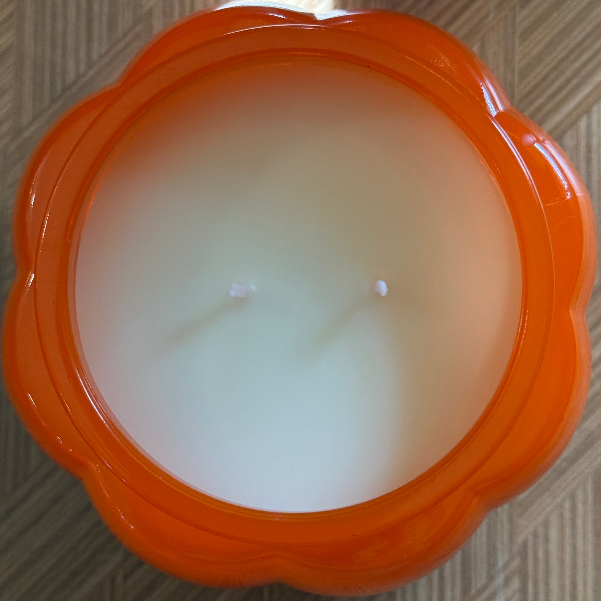 Orange pumpkin candle showing the candle surface with two wicks  on a textured surface