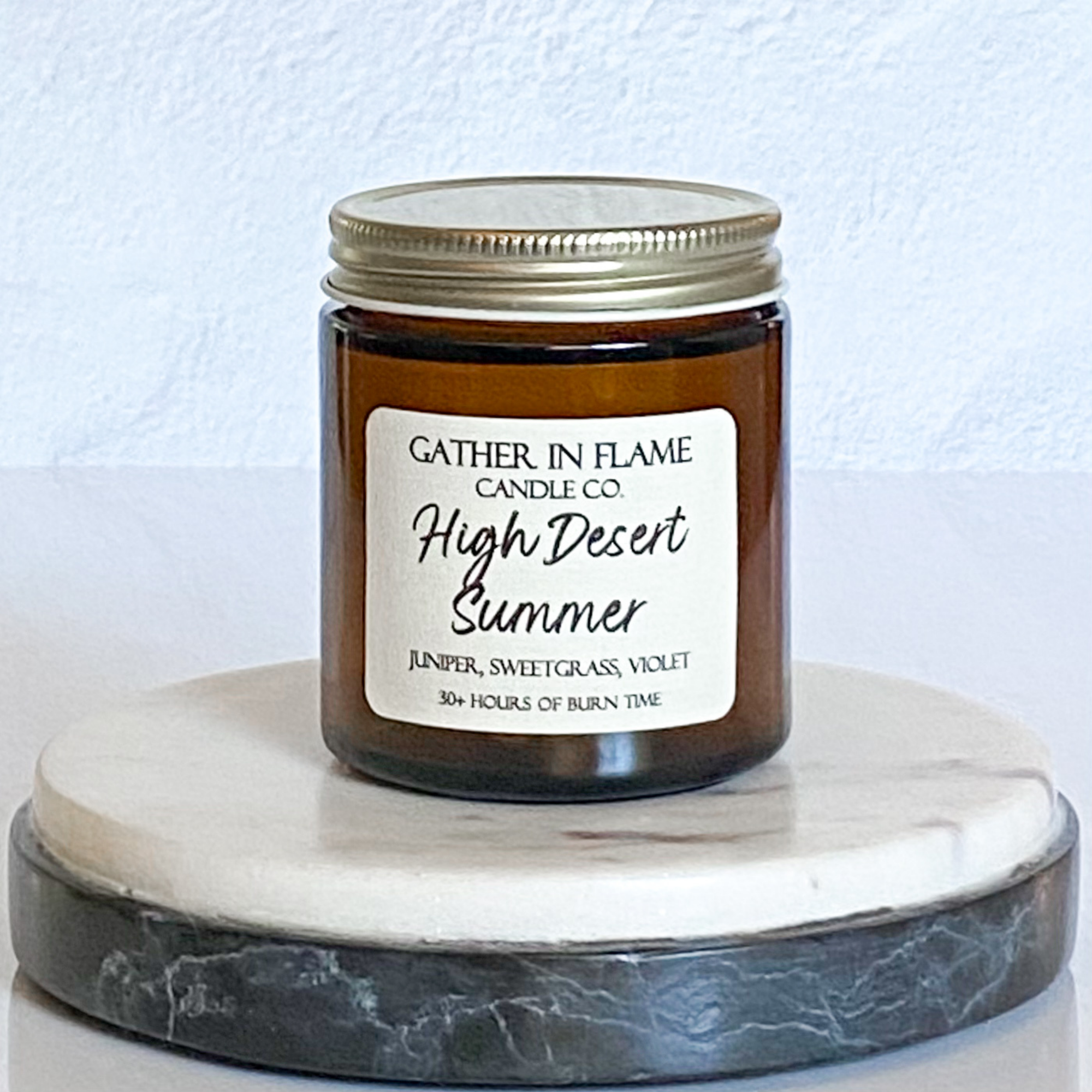 A jar candle with a label reading 'High Desert Summer', placed on a marble surface.