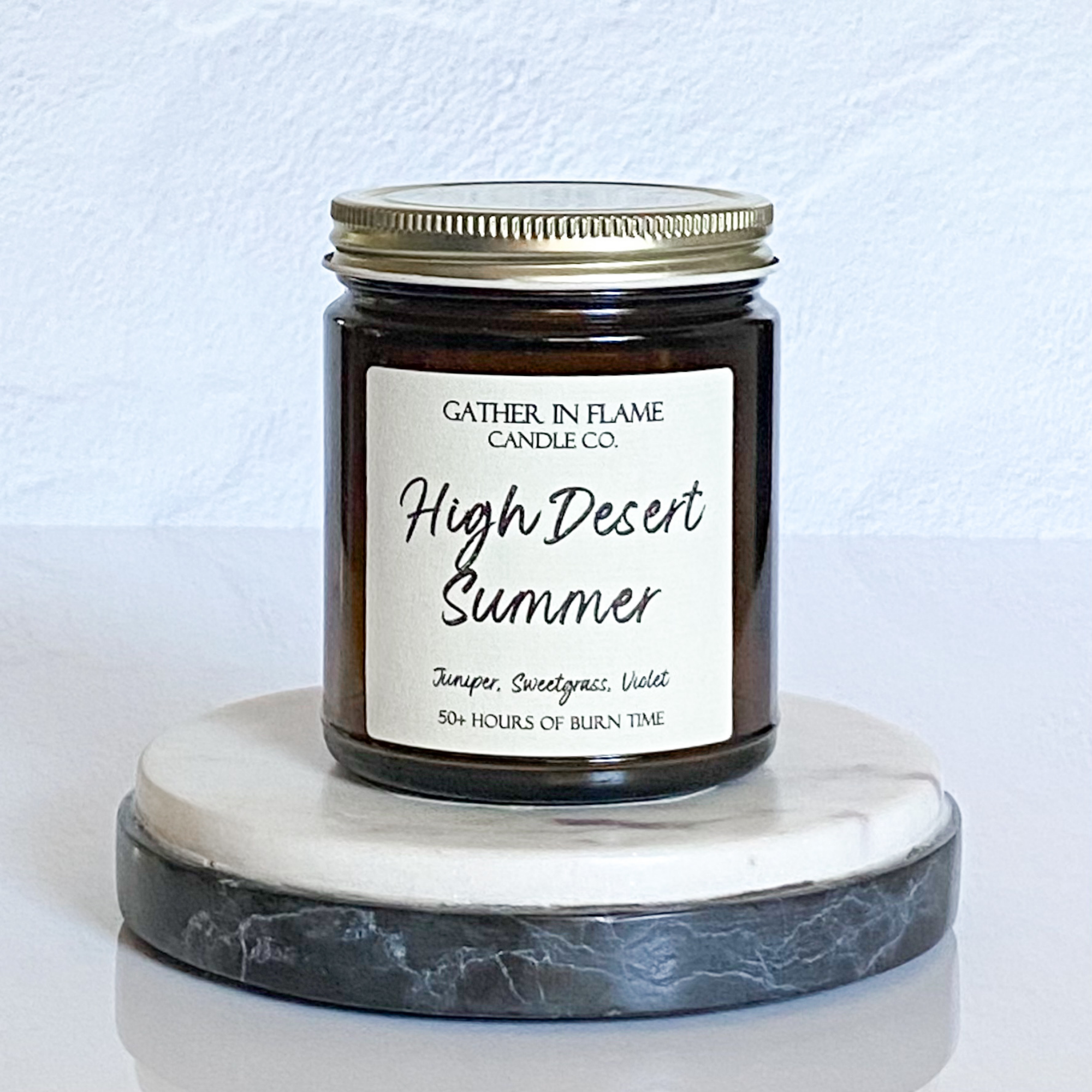 A jar candle with a label reading 'High Desert Summer', placed on a marble surface.