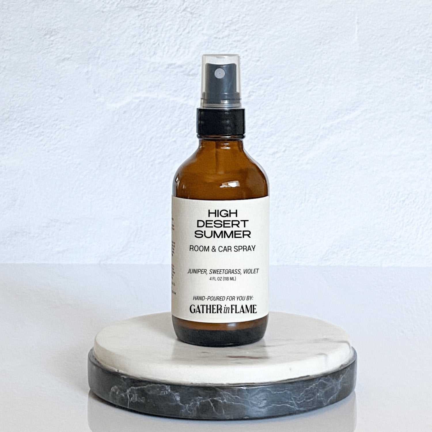 A brown amber spray bottle labeled 'High Desert Summer' by Gather In Flame Candle Co. on a white marble surface.