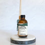 Amber glass reed diffuser bottle labeled Home for the Holidays wrapped in a green ribbon, placed on a marble coaster with a white background