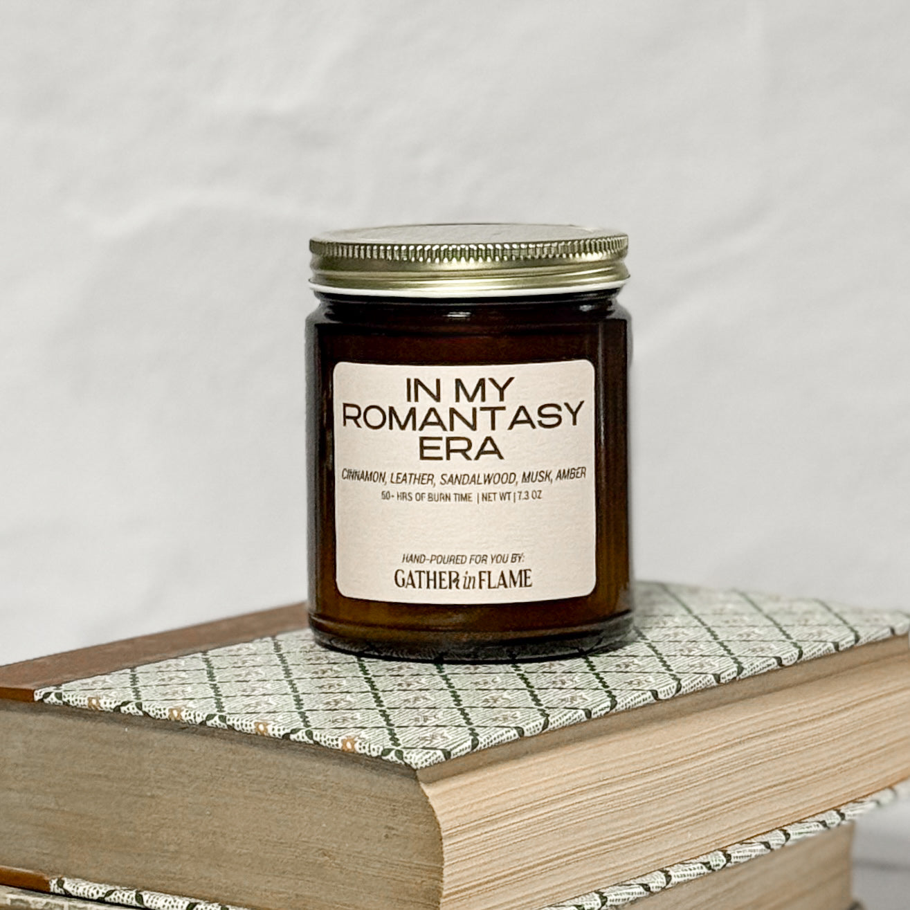 Amber glass jar candle labeled In My Romantasy Era on a stack of books with a white background.