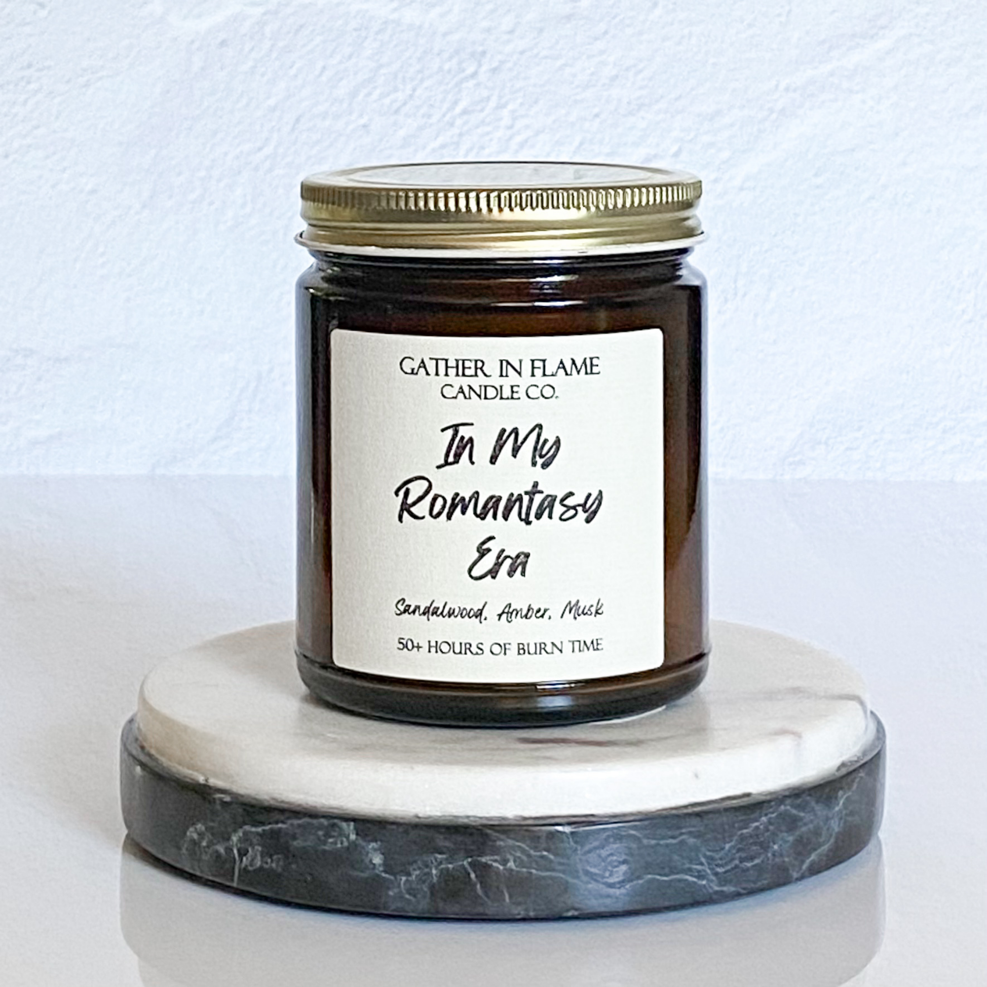 A jar candle with a white label that reads 'In My Romantasy Era', placed on a marble surface.