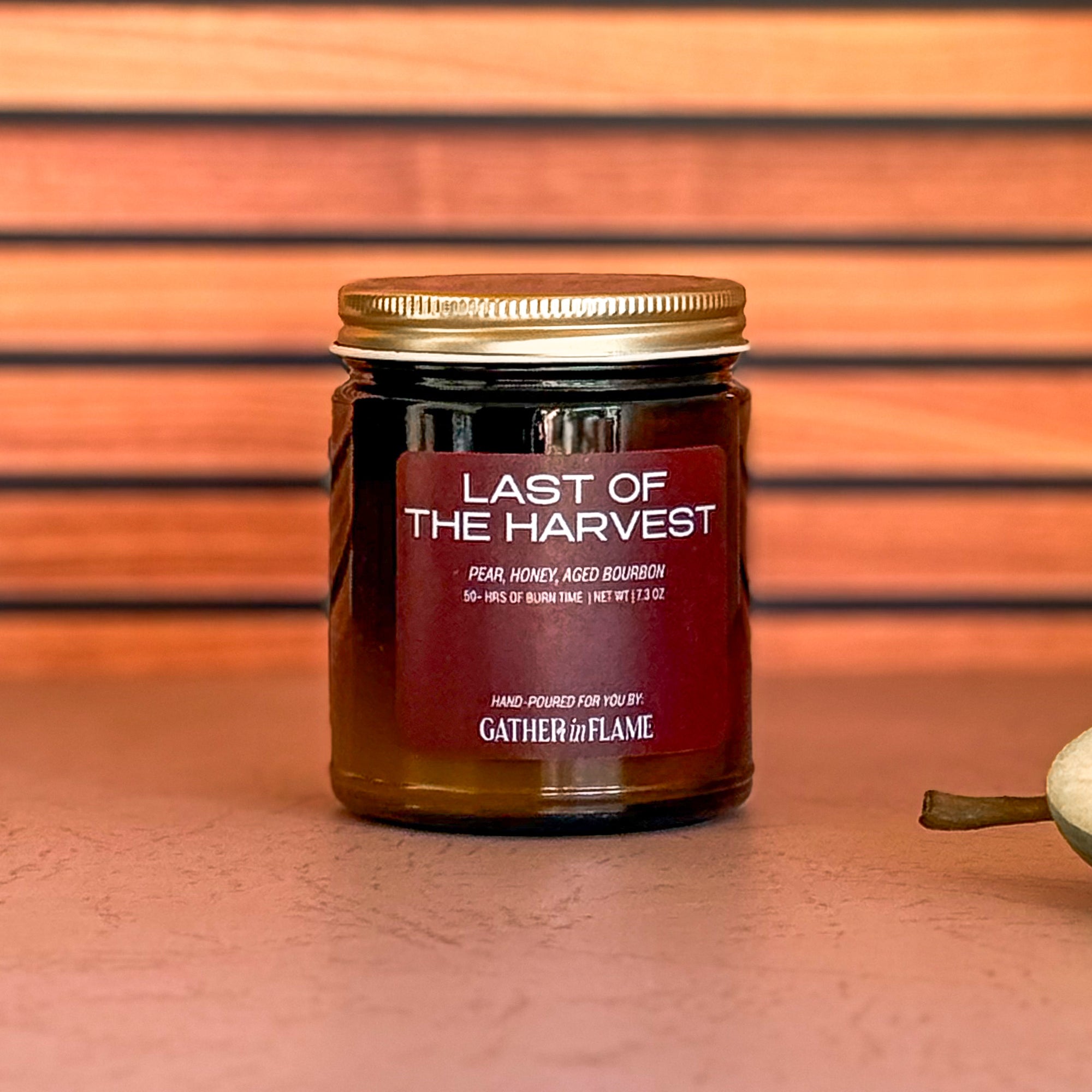 Jar of &#39;Last of the Harvest&#39; candle with a wooden wick on a striped background