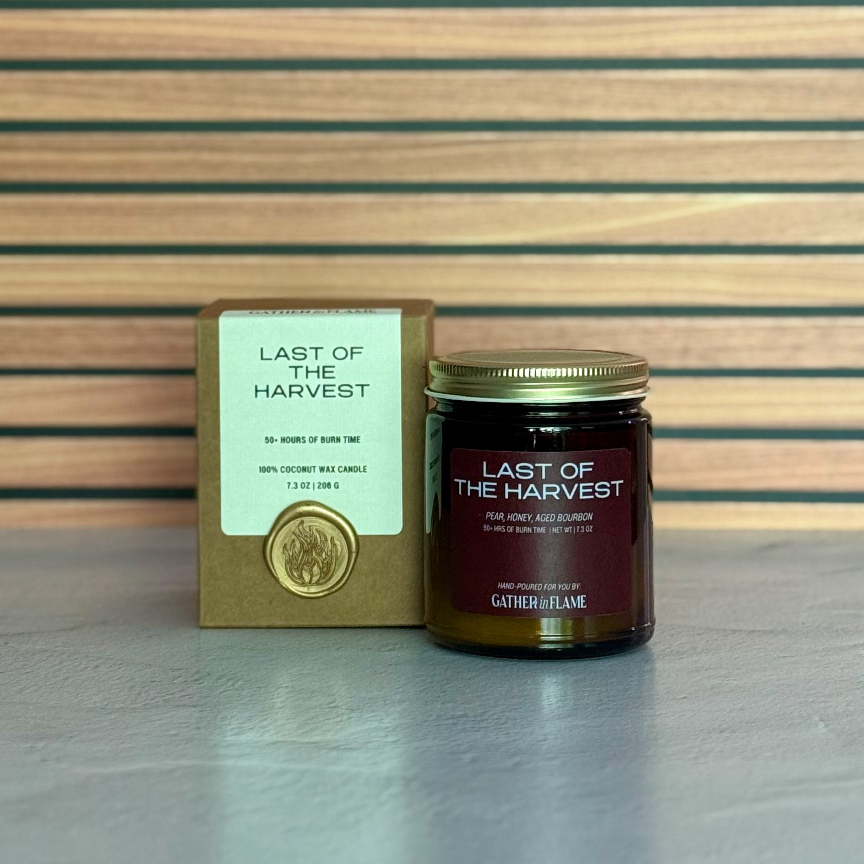 Candle labeled &#39;Last of the Harvest&#39; with packaging on a striped background