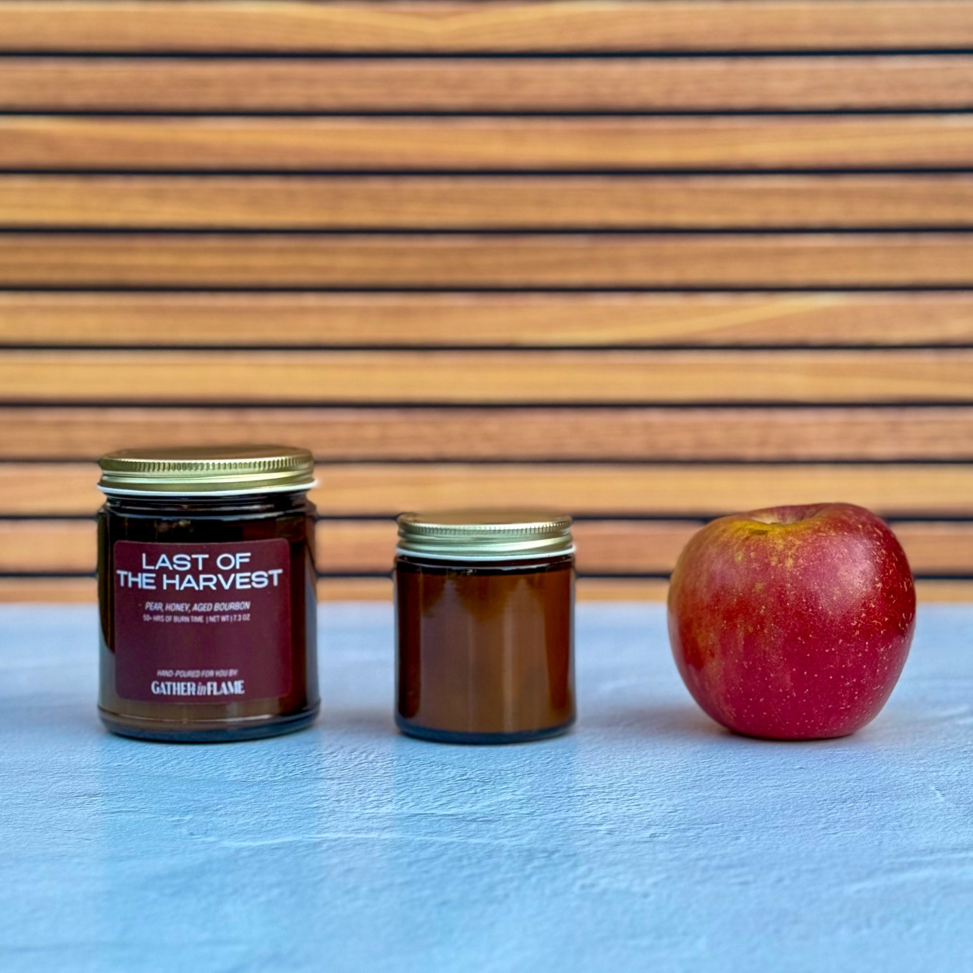 Two candles of different sizes and an apple on a light blue surface with a wooden background