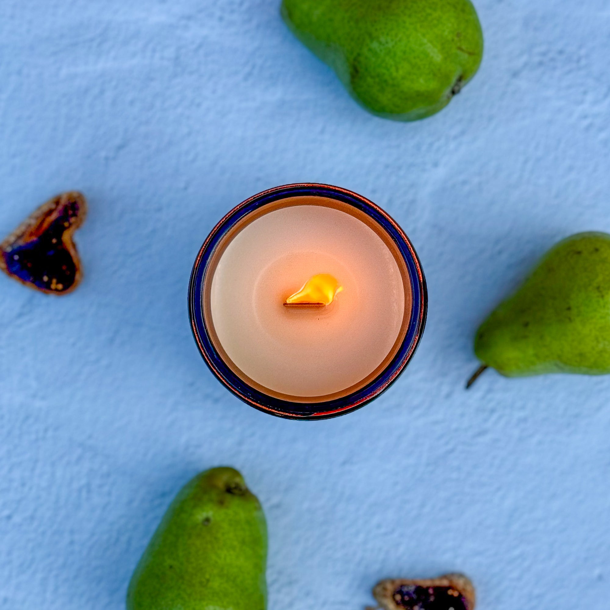 topdown view of lit candle in a decorative holder with pears on a light blue surface