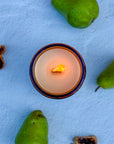topdown view of lit candle in a decorative holder with pears on a light blue surface