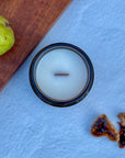 Topdown view of candle with wood wick on a textured blue surface with a pear and fig slices.