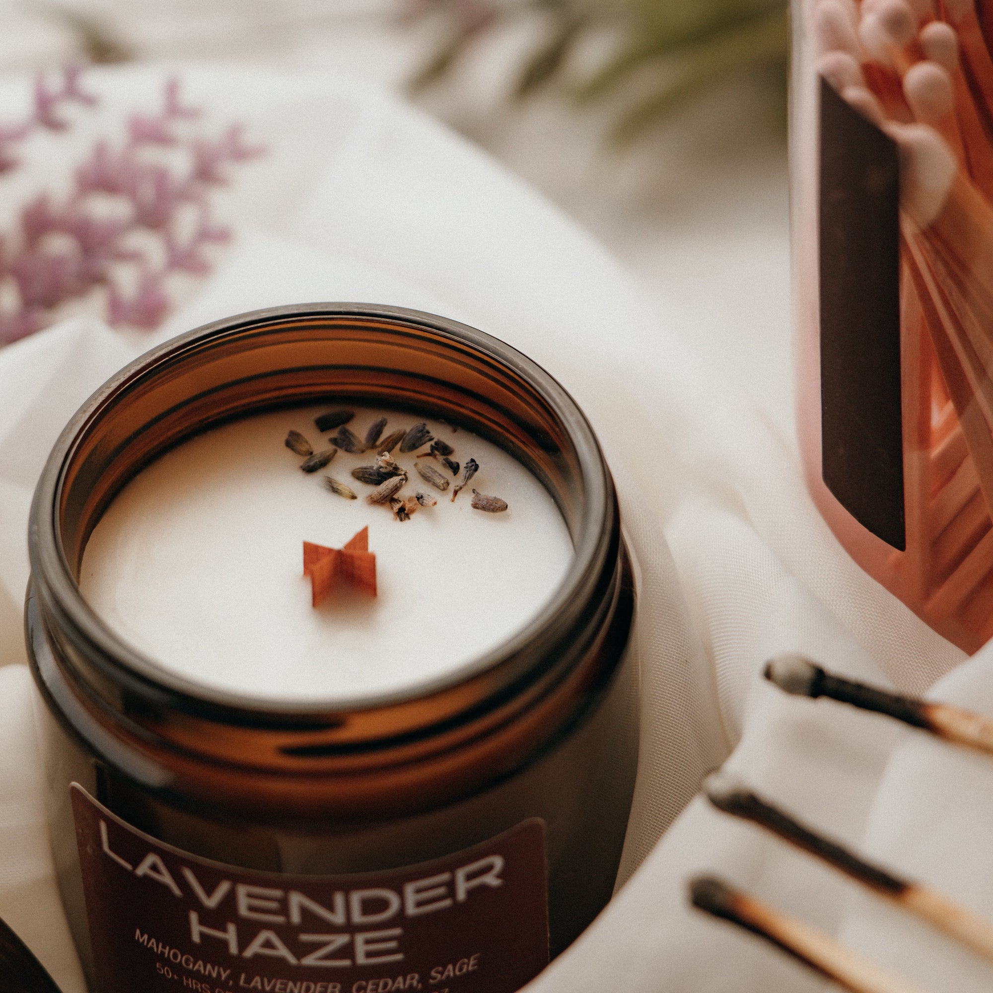 Candle jar labeled 'Lavender Haze' with lavender flowers and matches in the background