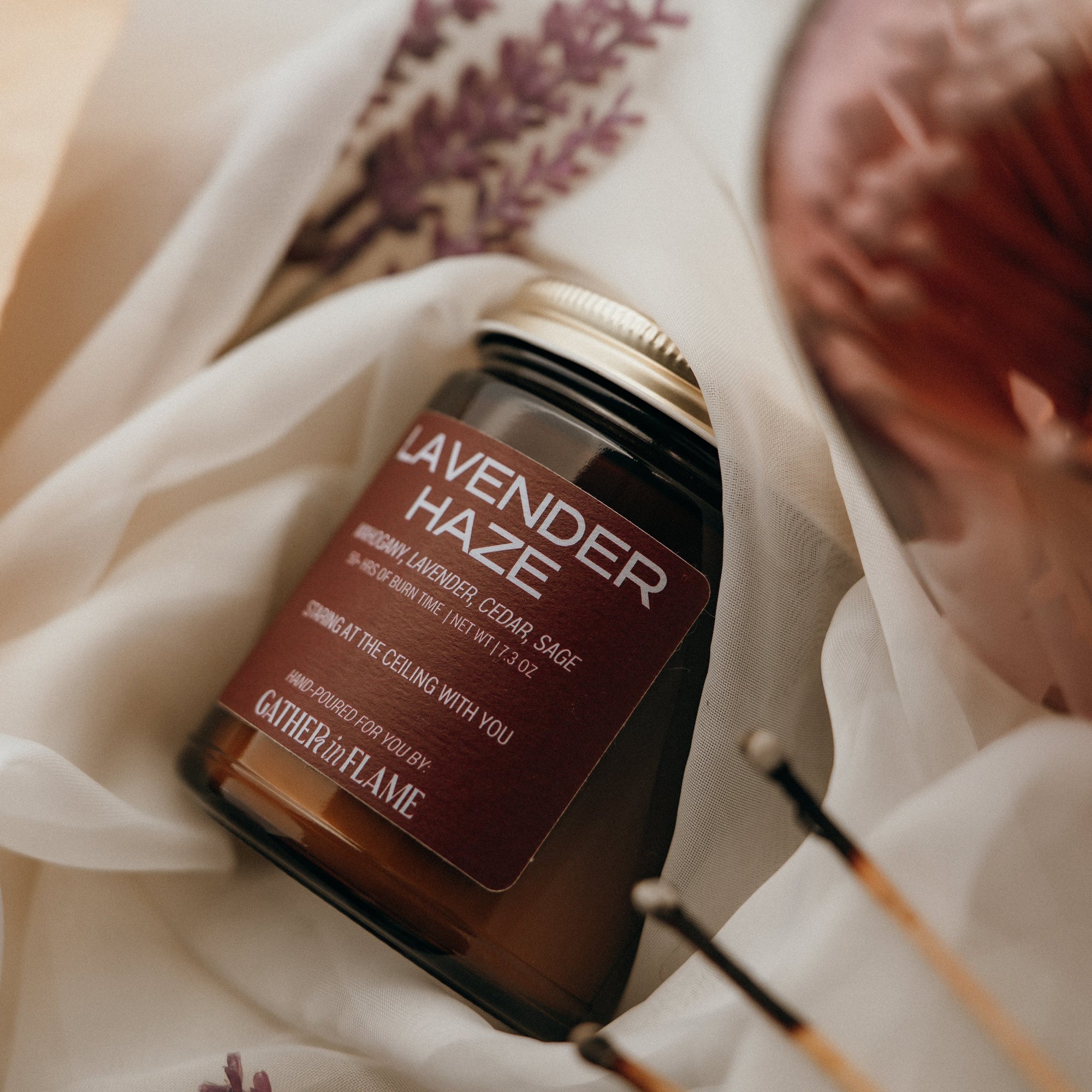 Jar of 'Lavender Haze' candle with decorative elements on a light fabric background