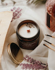 Candle in a jar with lavender scent on a white surface with matches and a book.