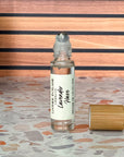 A perfume oil roller with a clear glass body and a bamboo cap sitting beside it, labeled 'Lavender Haze' on a terrazzo surface with wood background.