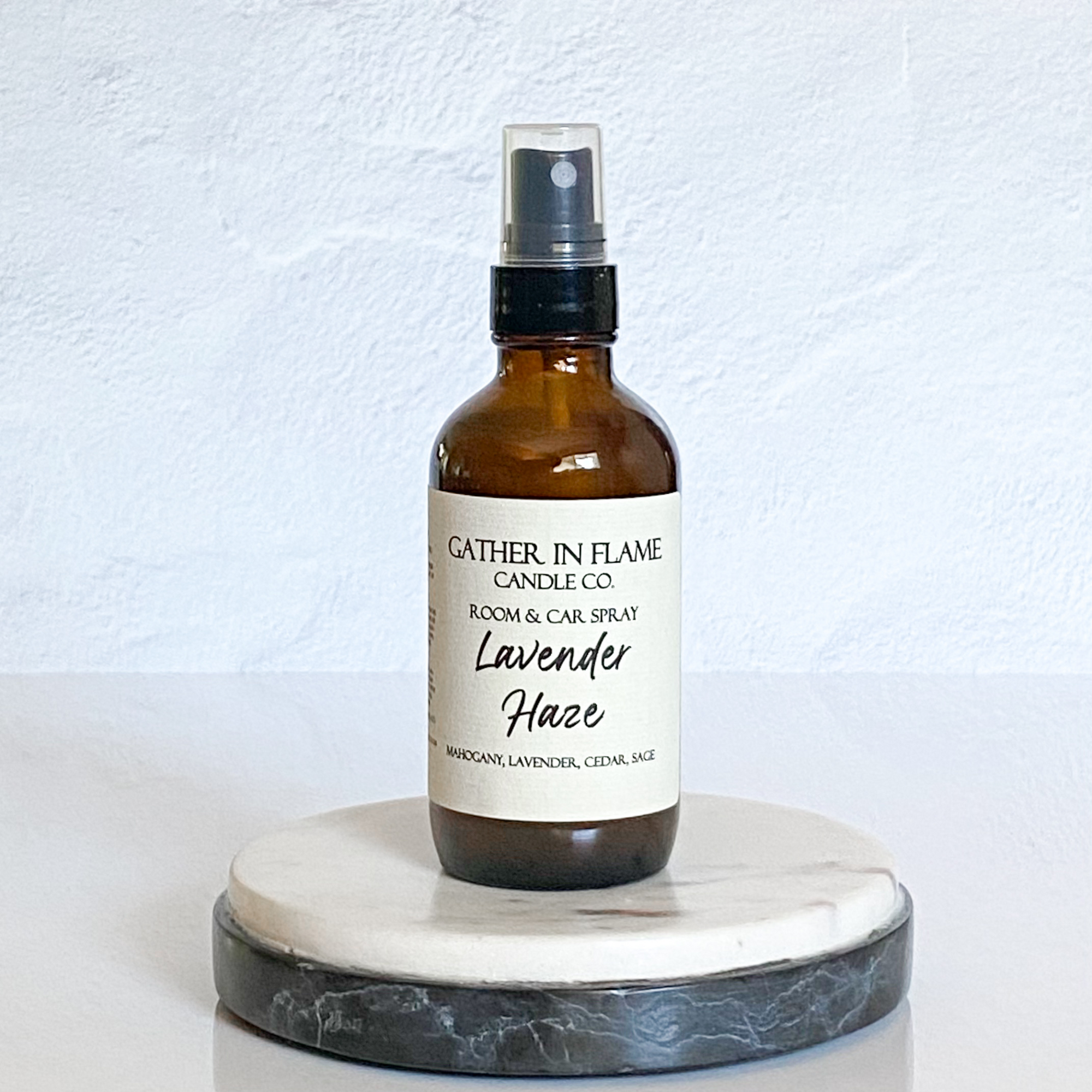 A brown amber spray bottle labeled 'Lavender Haze' by Gather In Flame Candle Co. on a white marble surface.