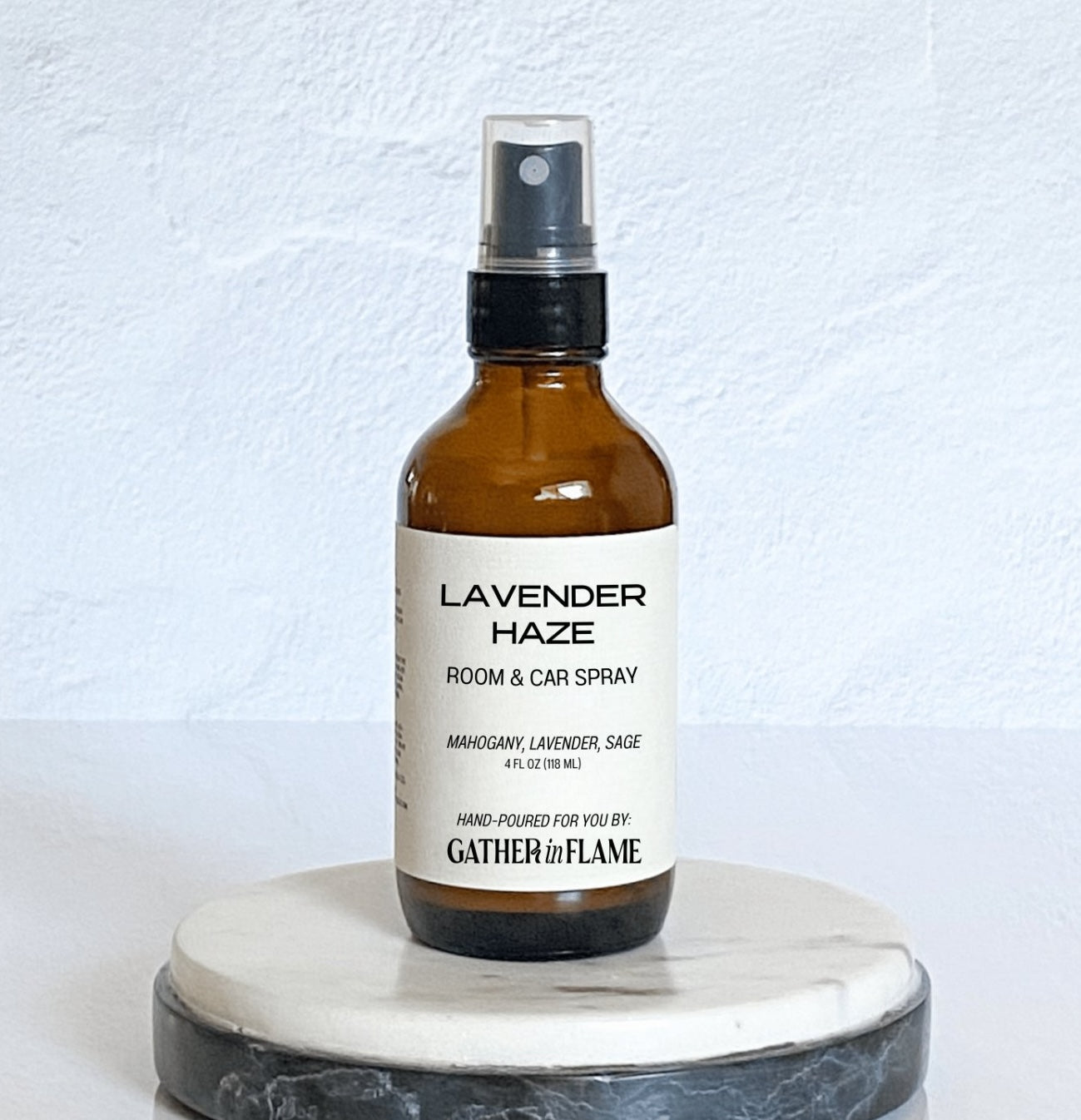 Amber glass room spray bottle labeled Gather in Flame Candle Co Lavender Haze on a gray marble coaster with a white background