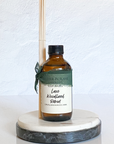 A brown reed diffuser bottle with a label reading 'Luxe Woodland Retreat', set on a white marble round tray with a green ribbon decoration.