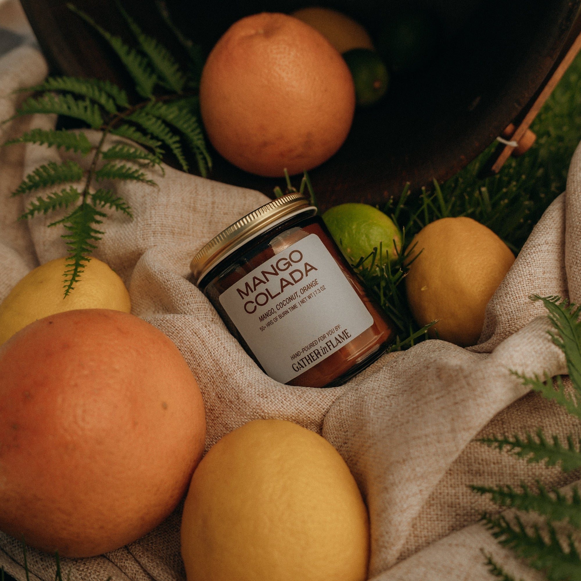 Jar of Mango Colada surrounded by mangoes on a textured surface with greenery