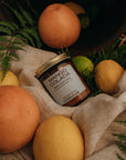 Jar of Mango Colada surrounded by mangoes on a textured surface with greenery