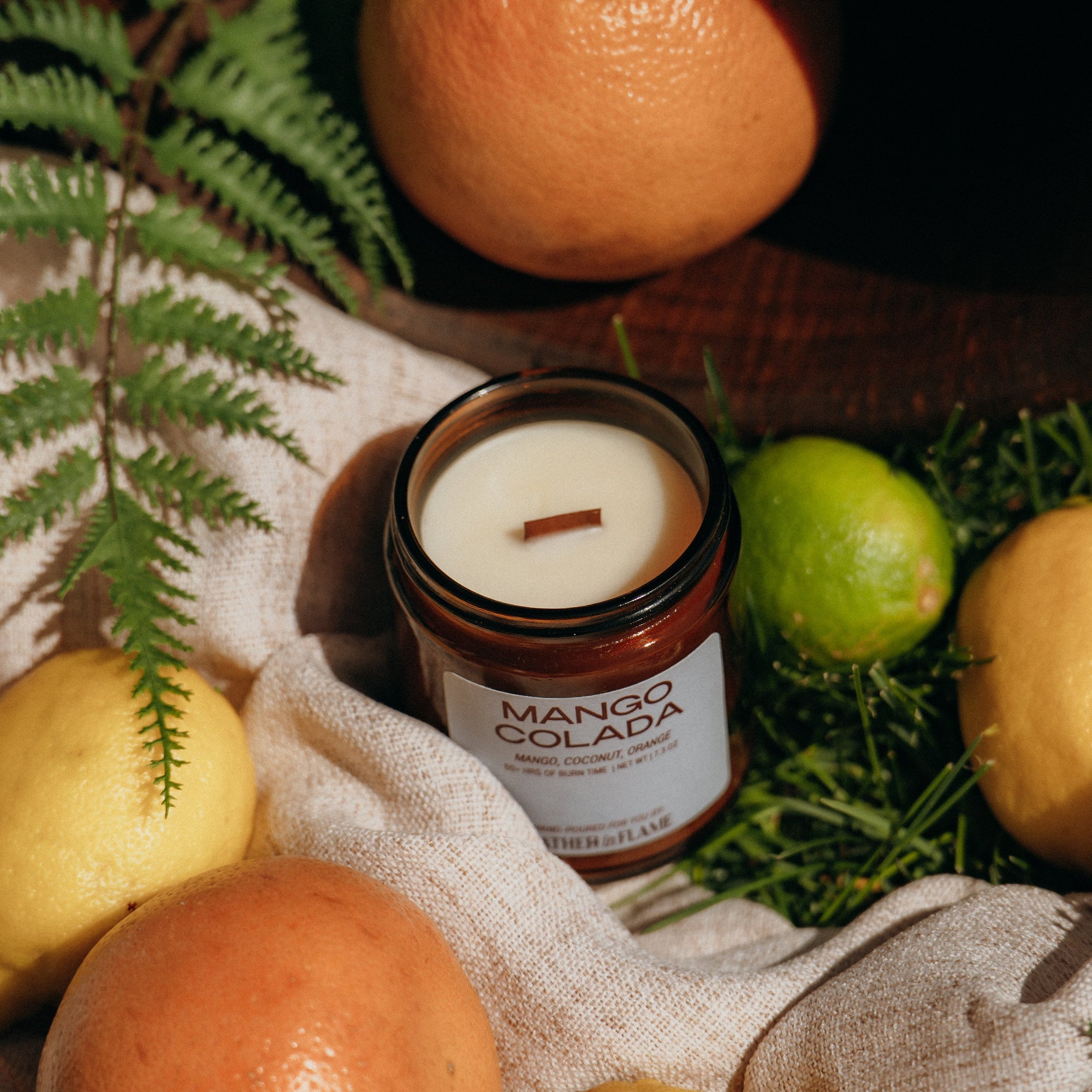 Mango Colada candle surrounded by fruits and foliage on a textured surface