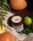 Mango Colada candle surrounded by fruits and foliage on a textured surface