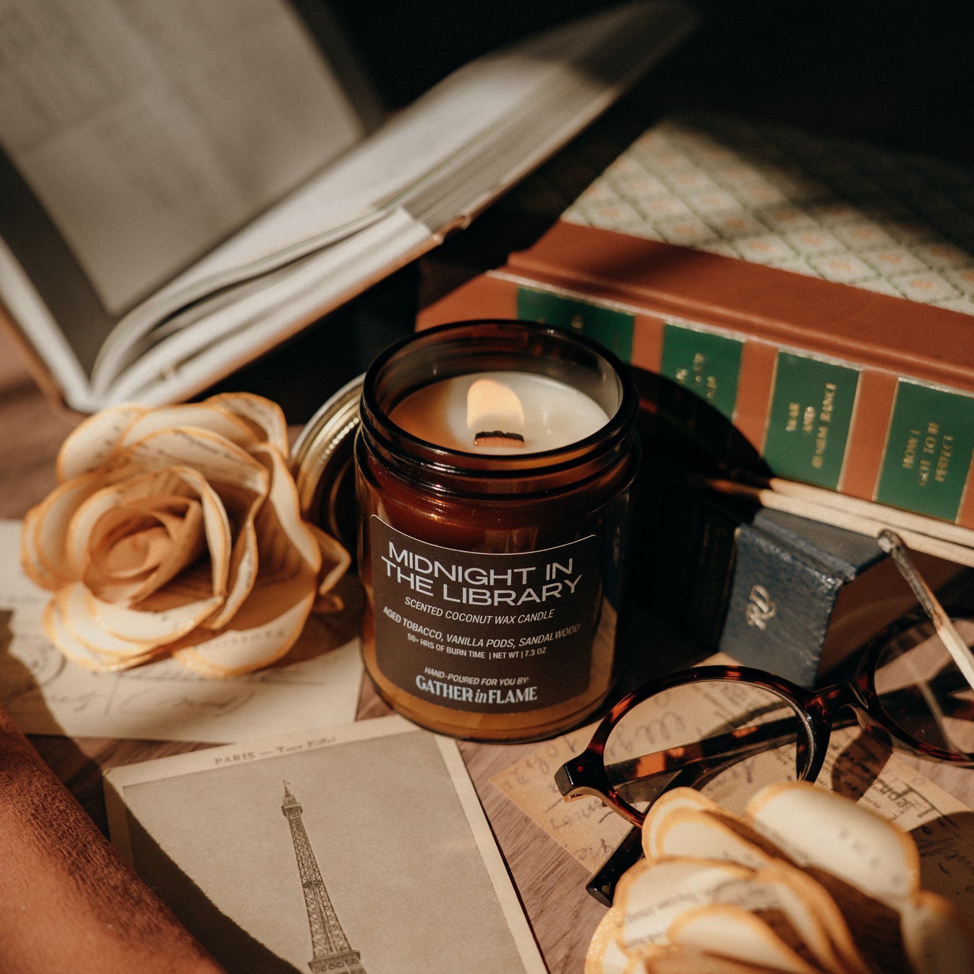 Candle labeled 'Midnight in the Library' on a surface with books, roses, and an open book.