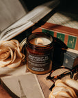 Candle labeled 'Midnight in the Library' on a surface with books, roses, and an open book.