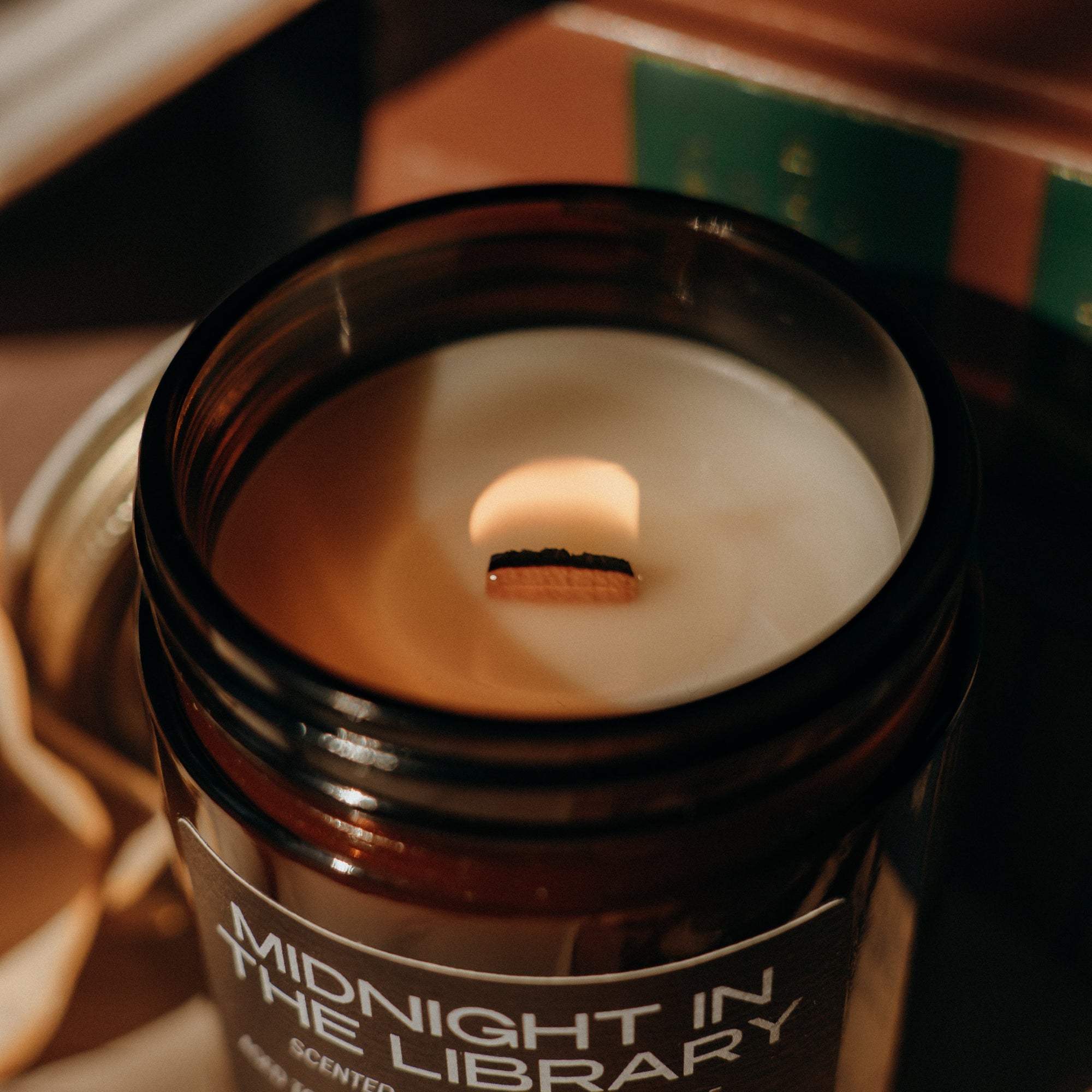 Candle in a jar labeled 'Midnight in the Library' on top of books.