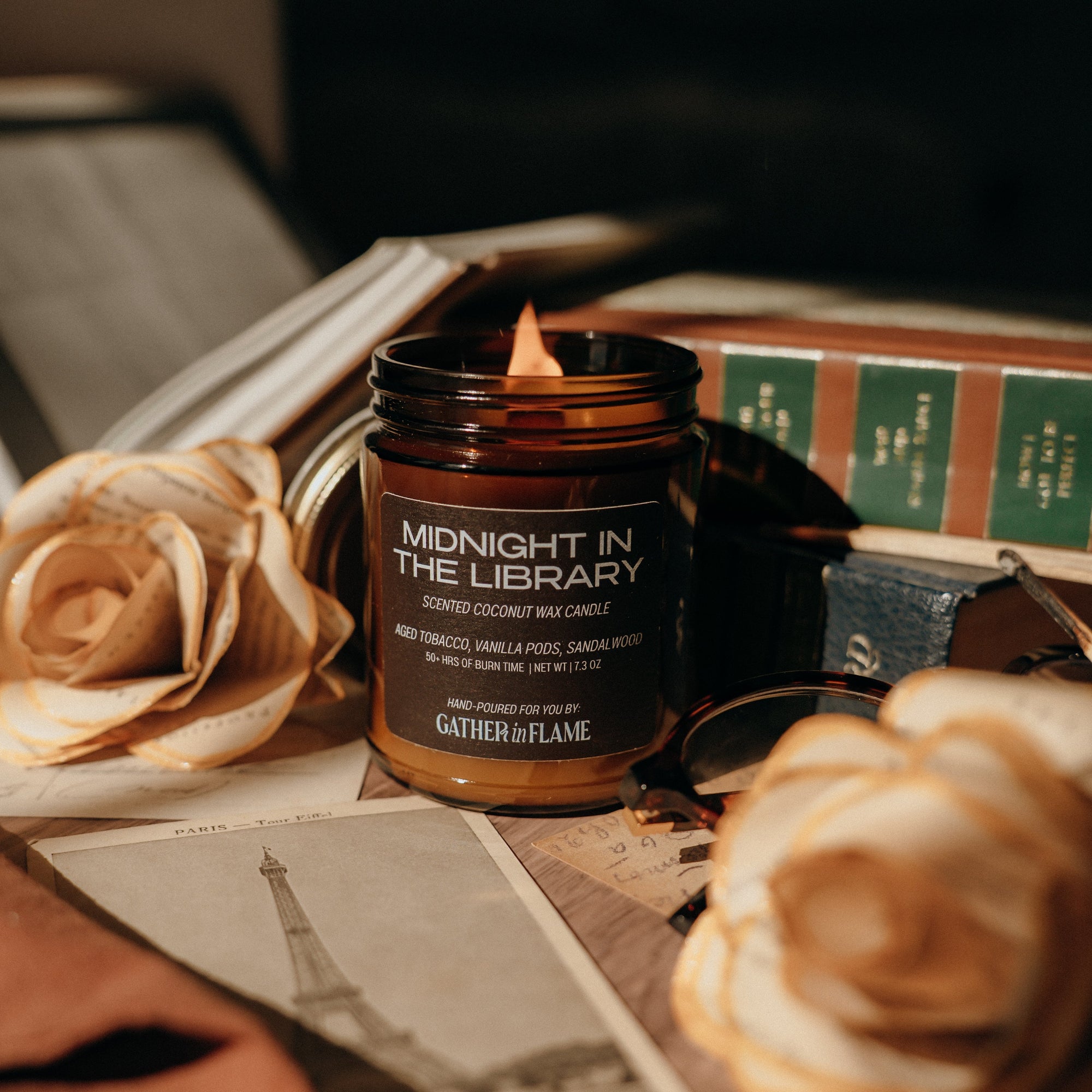 Candle labeled 'Midnight in the Library' on a surface with books and flowers.