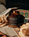 Candle labeled 'Midnight in the Library' on a surface with books and flowers.