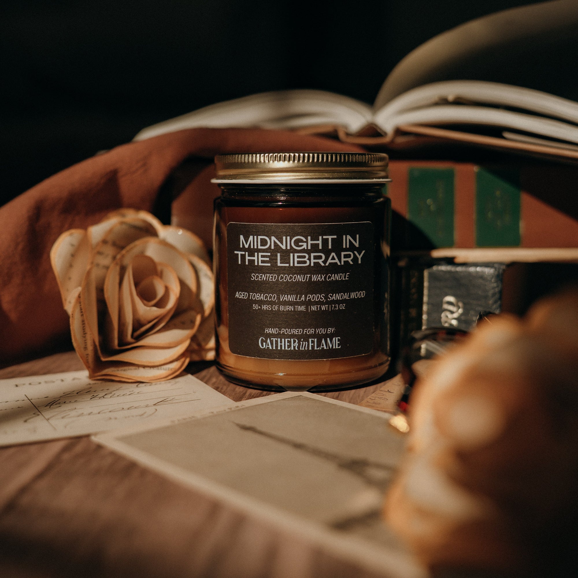 Candle jar labeled 'Midnight in the Library' on a surface with a rose and book in the background.