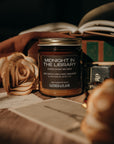 Candle jar labeled 'Midnight in the Library' on a surface with a rose and book in the background.