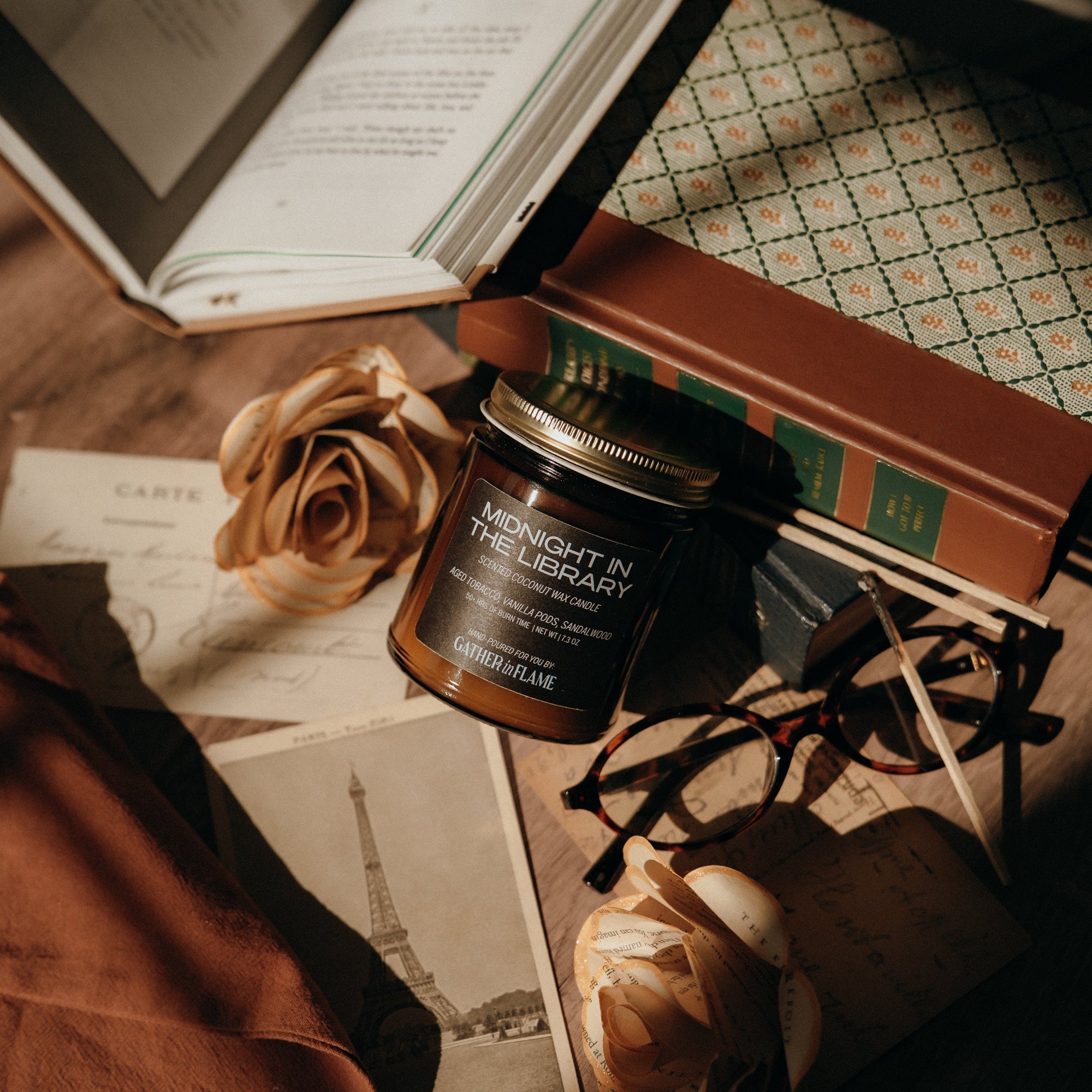 Jar of 'Midnight in the Library' candle on a book with roses and glasses