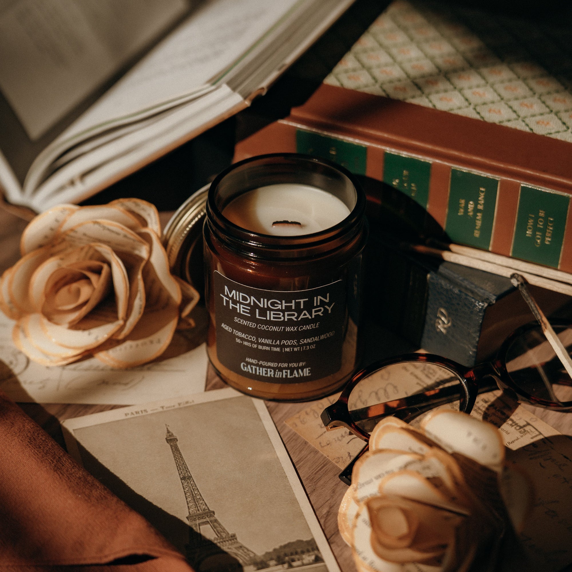 Candle labeled 'Midnight in the Library' on a desk with books, roses, and a map.