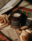 Candle labeled 'Midnight in the Library' on a desk with books, roses, and a map.