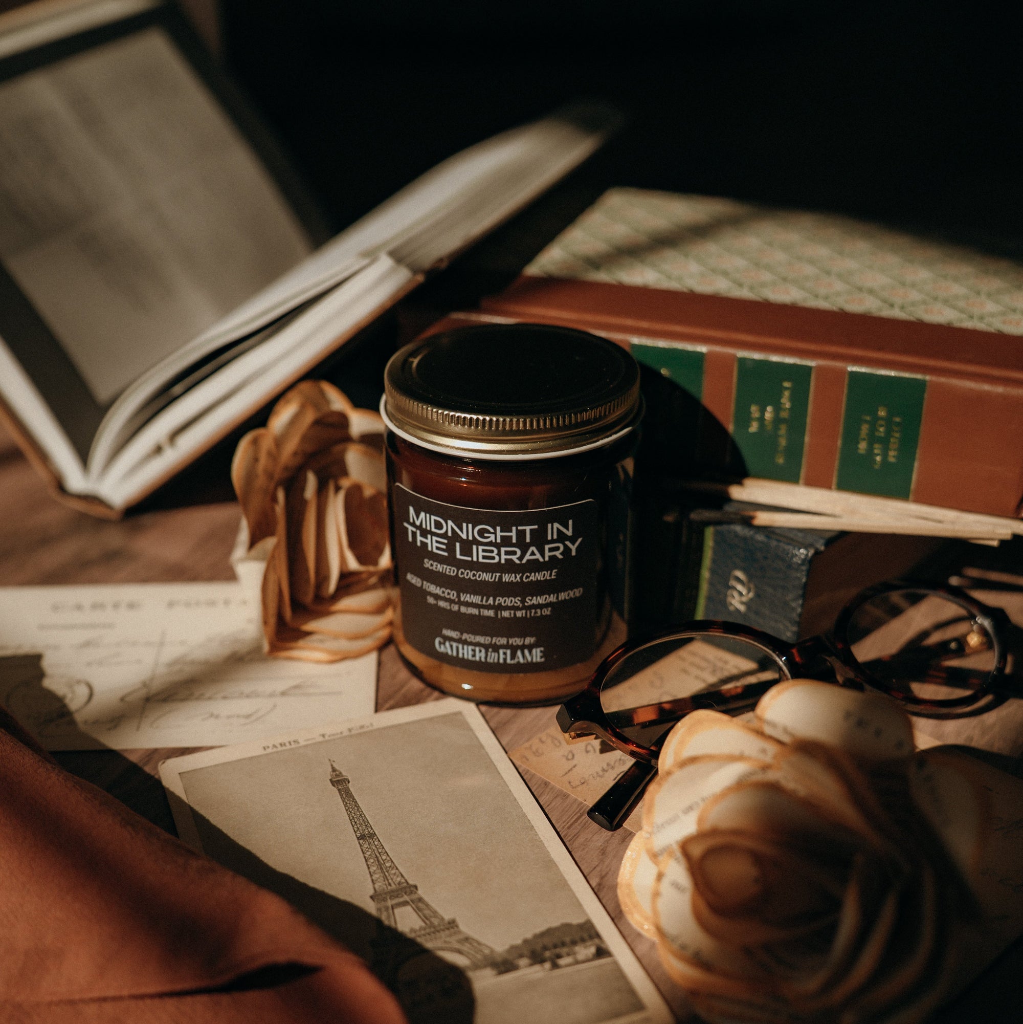 Candle labeled 'Midnight in theLibrary' on a surface with books and a rose.